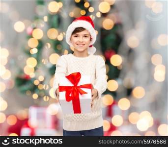 holidays, presents, christmas, childhood and people concept - smiling happy boy in santa hat with gift box over lights background