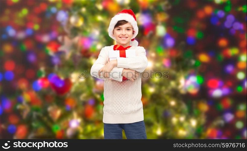 holidays, presents, christmas, childhood and people concept - smiling happy boy in santa hat with gift box over holidays lights background