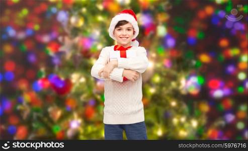 holidays, presents, christmas, childhood and people concept - smiling happy boy in santa hat with gift box over holidays lights background