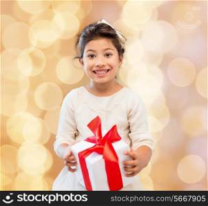holidays, presents, christmas, childhood and people concept - smiling little girl girl with gift box over beige lights background