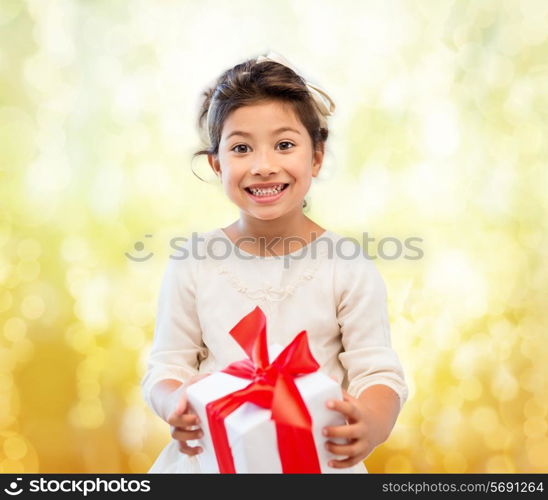 holidays, presents, christmas, childhood and people concept - smiling little girl girl with gift box over yellow lights background