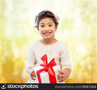 holidays, presents, christmas, childhood and people concept - smiling little girl girl with gift box over yellow lights background