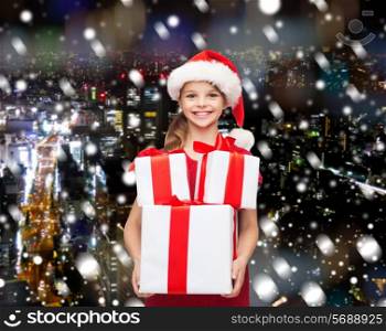 holidays, presents, christmas, childhood and people concept - smiling little girl in santa helper hat with gift boxes over snowy night city background