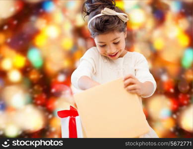 holidays, presents, christmas, childhood and people concept - smiling little girl with gift box over red lights background