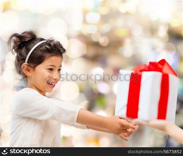 holidays, presents, christmas, childhood and people concept - smiling little girl with gift box over lights background