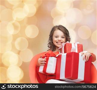 holidays, presents, christmas, childhood and people concept - smiling little girl with gift boxes over beige lights background