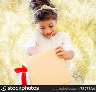 holidays, presents, christmas, childhood and people concept - smiling little girl with gift box over yellow lights background