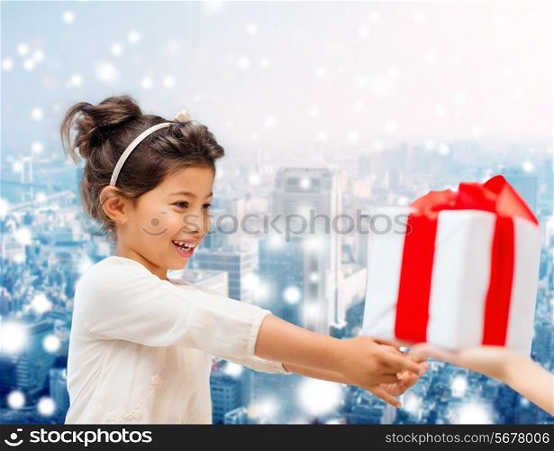 holidays, presents, christmas, childhood and people concept - smiling little girl with gift box over snowy city background