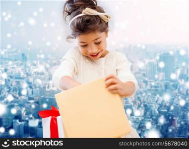 holidays, presents, christmas, childhood and people concept - smiling little girl with gift box over snowy city background