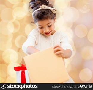 holidays, presents, christmas, childhood and people concept - smiling little girl with gift box over beige lights background