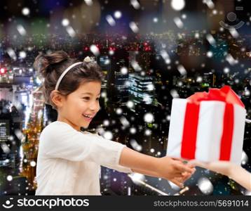 holidays, presents, christmas, childhood and people concept - smiling little girl with gift box over snowy night city background