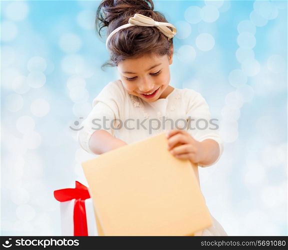 holidays, presents, christmas, childhood and people concept - smiling little girl with gift box over blue lights background