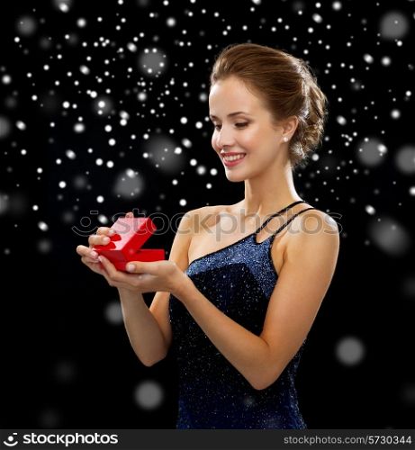 holidays, presents, luxury and happiness concept - smiling woman in dress holding red gift box over black snowy background
