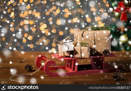 holidays, presents, new year and celebration concept - close up of gift boxes with blank note on red wooden sleigh over christmas tree and lights background