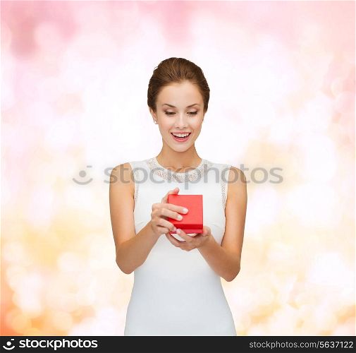 holidays, presents, wedding and happiness concept - smiling woman in white dress holding red gift box over pink lights background