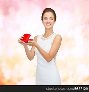 holidays, presents, wedding and happiness concept - smiling woman in white dress holding red gift box over pink lights background