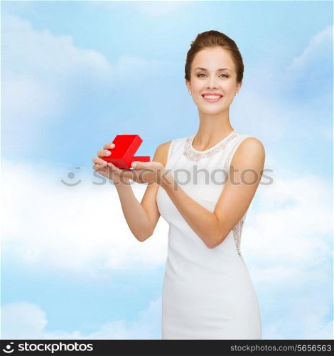 holidays, presents, wedding and happiness concept - smiling woman in white dress holding red gift box over blue cloudy sky background