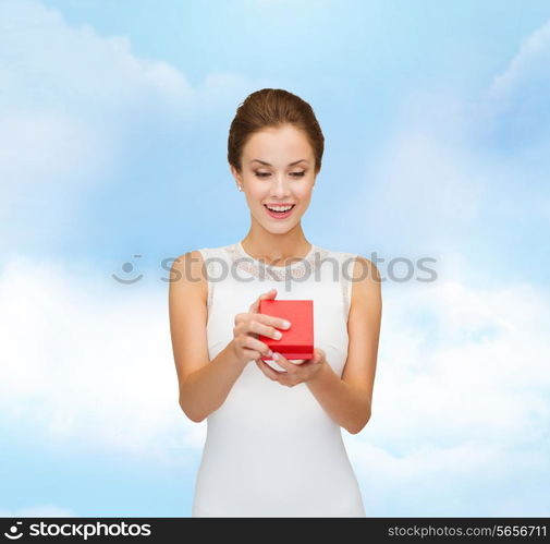 holidays, presents, wedding and happiness concept - smiling woman in white dress holding red gift box over blue cloudy sky background