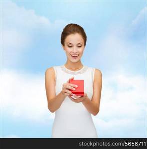 holidays, presents, wedding and happiness concept - smiling woman in white dress holding red gift box over blue cloudy sky background