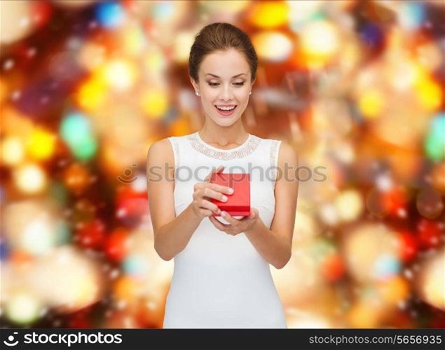 holidays, presents, wedding and happiness concept - smiling woman in white dress holding red gift box over party lights background