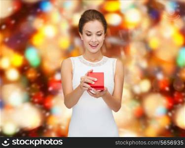 holidays, presents, wedding and happiness concept - smiling woman in white dress holding red gift box over party lights background