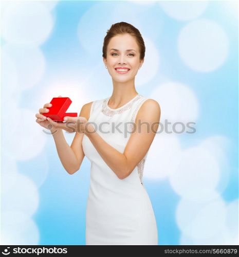holidays, presents, wedding and happiness concept - smiling woman in white dress holding red gift box over blue lights background