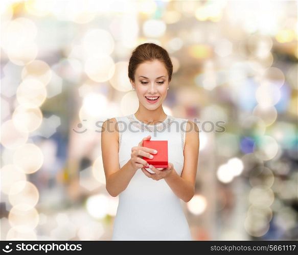 holidays, presents, wedding and happiness concept - smiling woman in white dress holding red gift box over shiny lights background