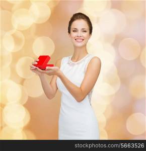holidays, presents, wedding and happiness concept - smiling woman in white dress holding red gift box over golden lights background