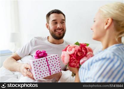 holidays, romance and people concept - happy couple with gift box in bed at home. happy couple with gift box in bed at home