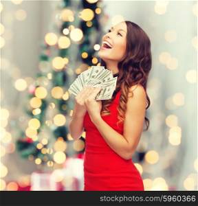 holidays, sale, banking and people concept - smiling woman in red dress with us dollar money over christmas tree lights background