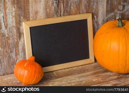 holidays, school and halloween concept - pumpkins with blank chalkboard on wooden boards background. blank chalkboard and halloween pumpkins