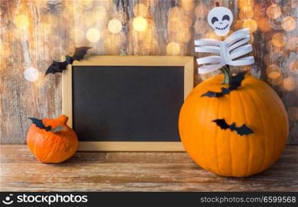 holidays, school and party concept - halloween pumpkins, decorations with blank chalkboard on wooden boards background. blank chalkboard and halloween decorations