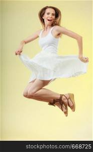 Holidays summer and happiness. Woman wearing white dress jumping. Female model in full length on yellow background.