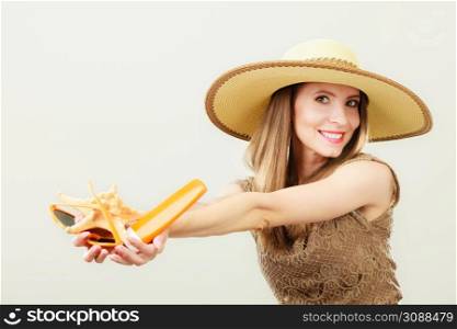 Holidays summer fashion and skin care concept. Woman in straw hat holds sunglasses shell and sunscreen lotion, gray background copy space