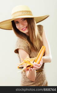 Holidays summer fashion and skin care concept. Woman in straw hat holds sunglasses shell and sunscreen lotion, gray background