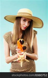 Holidays summer fashion and skin care concept. Woman in straw hat holds sunglasses shell and sunscreen lotion, blue background