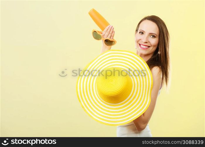 Holidays summer fashion. and skin care concept. Woman in yellow hat holds heart shaped sunglasses sunscreen lotion, bright background copy space