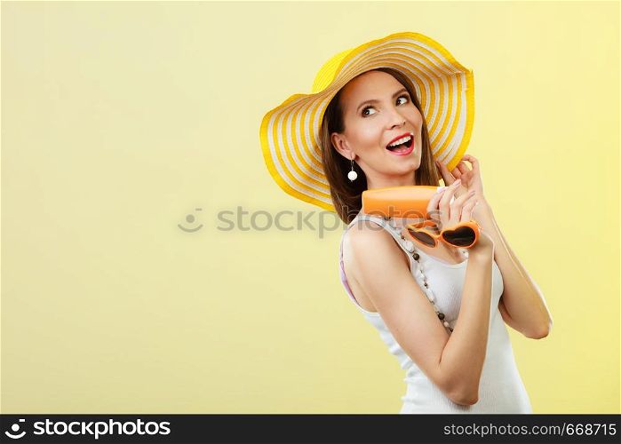 Holidays summer fashion. and skin care concept. Woman in yellow hat holds heart shaped sunglasses sunscreen lotion, bright background copy space