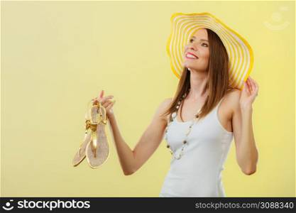 Holidays summer fashion concept. Woman in big yellow hat holding golden sandals in hand bright background.