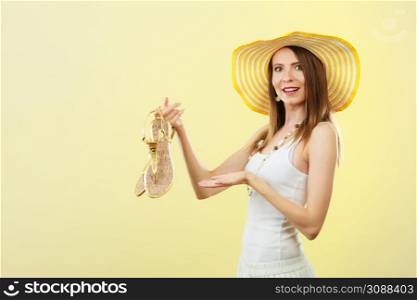 Holidays summer fashion concept. Woman in big yellow hat holding golden sandals in hand bright background.
