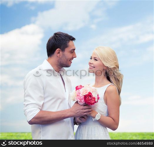 holidays, summer, people and dating concept - happy couple with bunch of flowers over blue sky and grass background