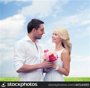 holidays, summer, people and dating concept - happy couple with bunch of flowers over blue sky and grass background