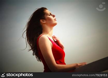 Holidays summer relaxation concept. Young thoughtful woman wearing red dress relaxing on pier outdoor