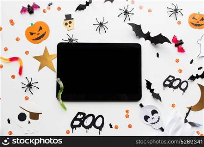 holidays, technology and party concept - halloween decorations and candies with tablet pc computer over white background. tablet pc, halloween party decorations and candies