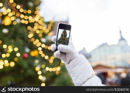 holidays, technology and people concept - hands with smartphone photographing christmas tree. hands with smartphone photographing christmas tree