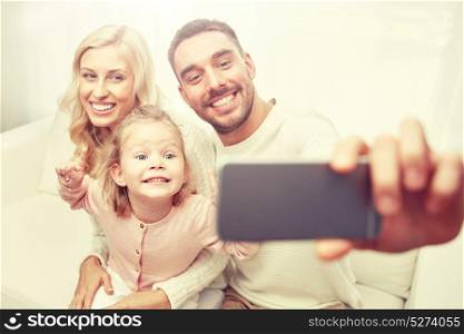 holidays, technology and people concept - happy family sitting on sofa and taking selfie picture with smartphone at home. family taking selfie with smartphone at home