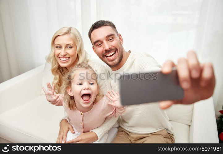 holidays, technology and people concept - happy family sitting on sofa and taking selfie picture with smartphone at home