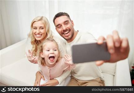 holidays, technology and people concept - happy family sitting on sofa and taking selfie picture with smartphone at home