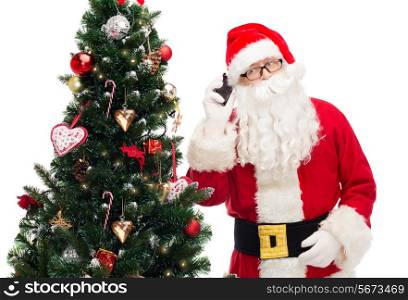 holidays, technology and people concept - man in costume of santa claus with smartphone and christmas tree