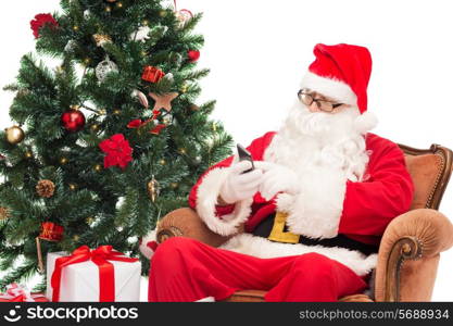 holidays, technology and people concept - man in costume of santa claus with smartphone, presents and christmas tree